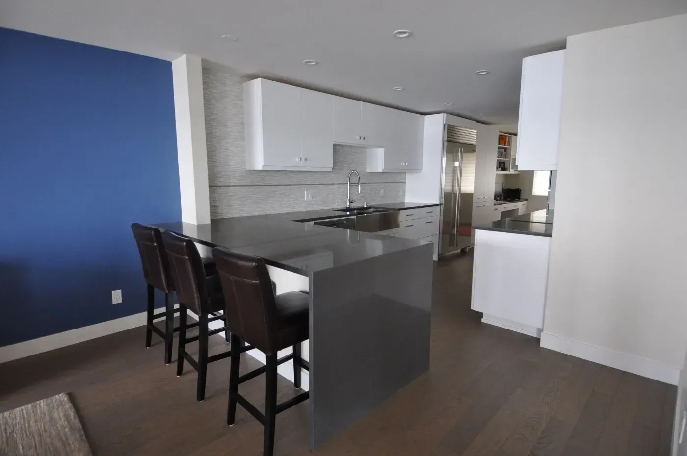 Modern kitchen with blue wall, gray island, white cabinets, and bar stools.