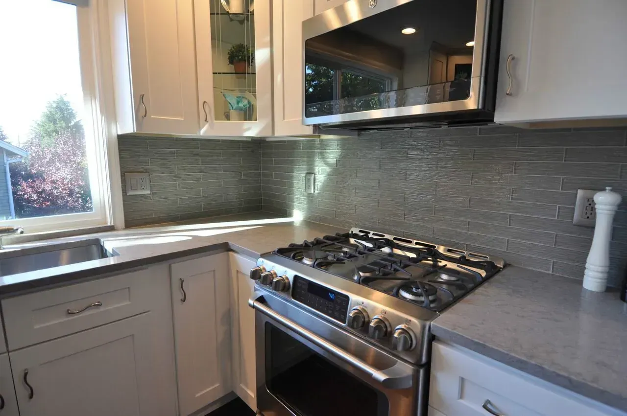 Kitchen with white cabinets, gray countertops, gas range, and gray tile backsplash.