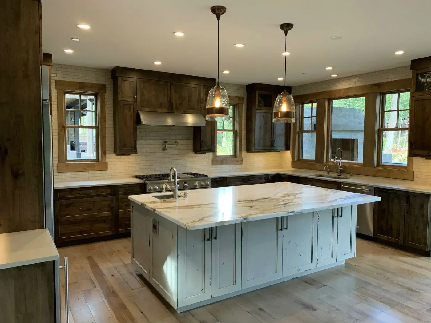 Kitchen with wooden cabinets, white island, marble countertops, and pendant lights.