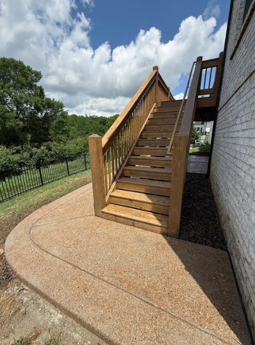 Outdoor wooden staircase beside a building, with a curved concrete path and fence under a cloudy sky