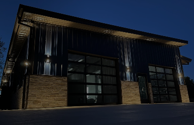Dark modern building with wood and metal exterior, lit by wall lamps at dusk.