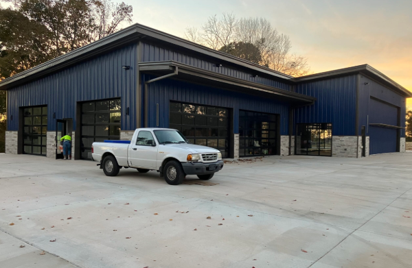 Blue metal building with large garage doors and a white pickup truck parked on a concrete lot at sunset