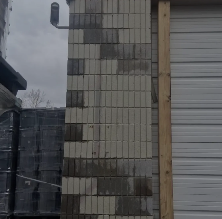 Damaged cinder block wall beside a white garage door with a wooden frame