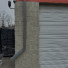 Gray brick wall with a downspout beside a closed metal garage door on a cloudy day
