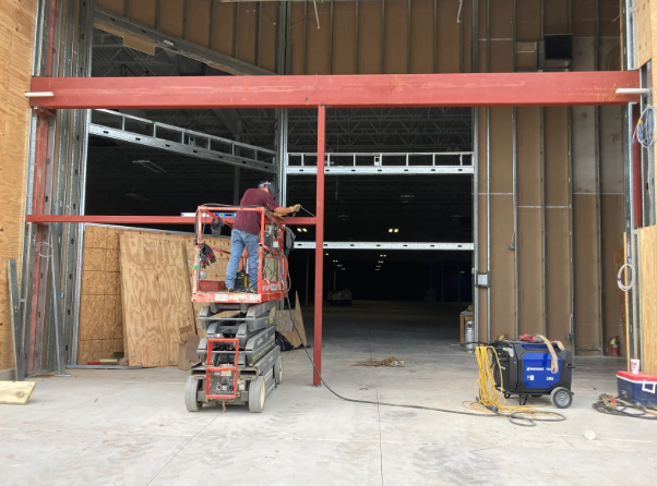 Person on a scissor lift working at a red-framed warehouse entrance with open, dark interior