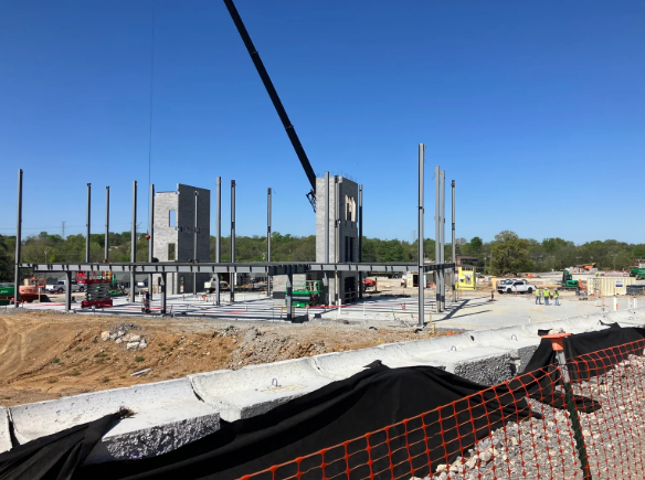 Construction site with crane, steel columns, and unfinished concrete foundations under a clear blue sky
