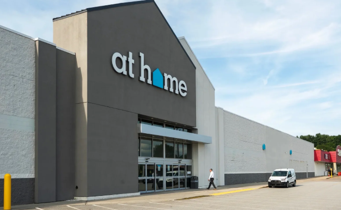 Athome store exterior with gray facade and glass entrance, parked car at right
