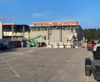 Construction site with green lift, scaffolding, and concrete block building under renovation