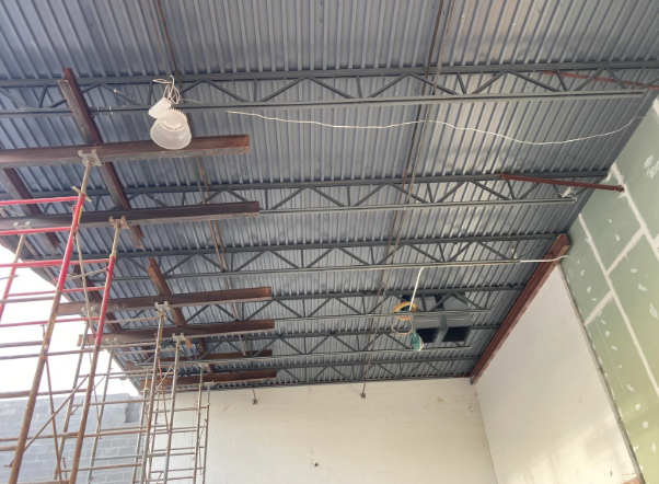 Interior of a warehouse under construction, showing a metal truss ceiling and scaffolding.
