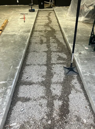 Narrow concrete trench with a rough resurfaced strip in an indoor construction area, bordered by metal rails
