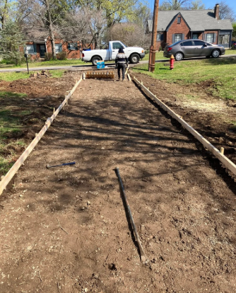 A dirt walkway under construction with wooden borders and a worker near a white truck in a neighborhood.