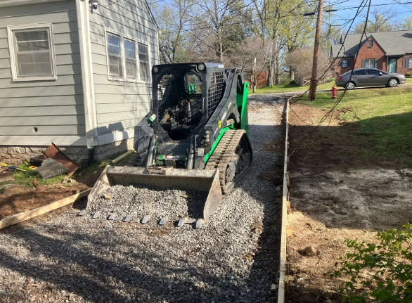 Skid steer loading gravel beside a house on a new driveway path