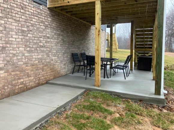 Covered patio with concrete slab, table and chairs, brick wall, and grassy yard view