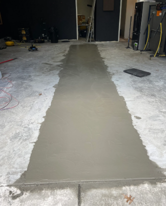Freshly poured gray concrete strip in a garage floor, surrounded by rough unfinished concrete.