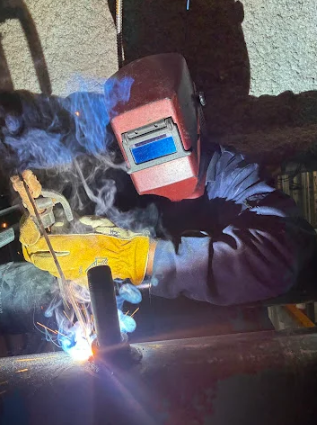 Welder in red helmet welding metal in a dim workshop, bright sparks and smoke visible