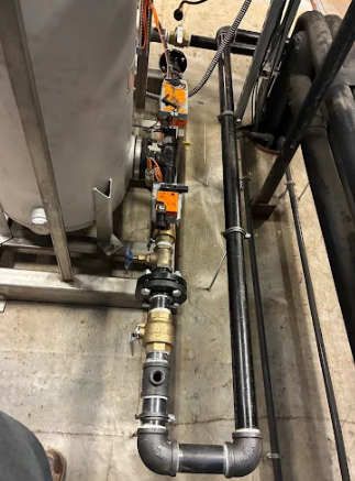 Industrial piping and valves beside a tank in a mechanical room