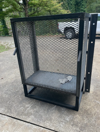 Black metal mesh cage on pavement with a hinged door and base platform.