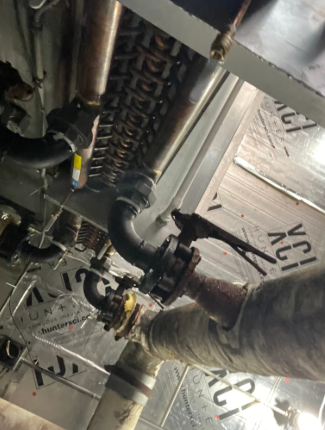 Worker handling black pipes inside a construction ceiling with metal framing and insulation