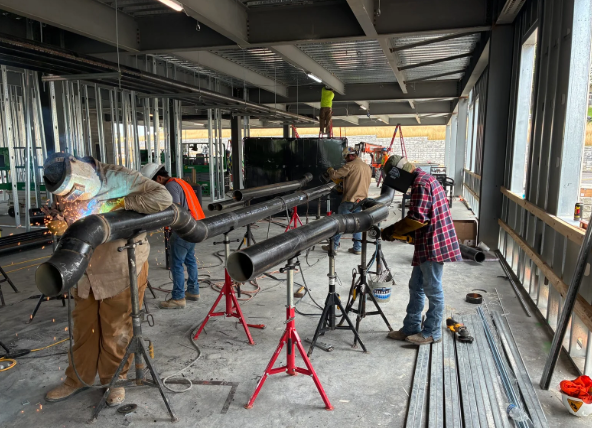Workers welding long metal pipes in an industrial workshop