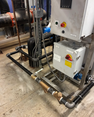 Industrial control panel and piping on a factory floor with black hoses and metal fittings.
