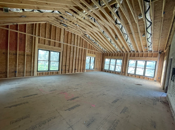 Framed interior of a new house under construction, with exposed roof trusses and large windows.