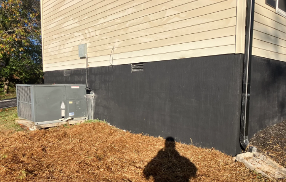House exterior with gray HVAC unit beside a black foundation and a pile of mulch in the yard