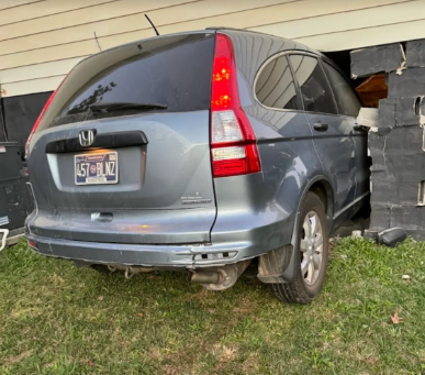 Gray Honda SUV backed into a damaged garage wall, with the rear wheel on grass.