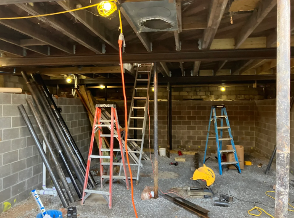 Construction site with ladders, tools, and exposed beams in a basement or crawlspace