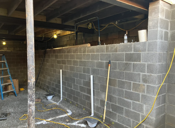 Basement under construction with cinder block wall, ladder, exposed beams, and hanging wires.
