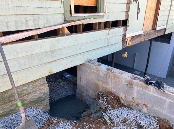 Crumbling house foundation with a large gap under the porch and exposed concrete supports.
