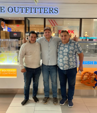 Three people standing together in a mall storefront, smiling at the camera.