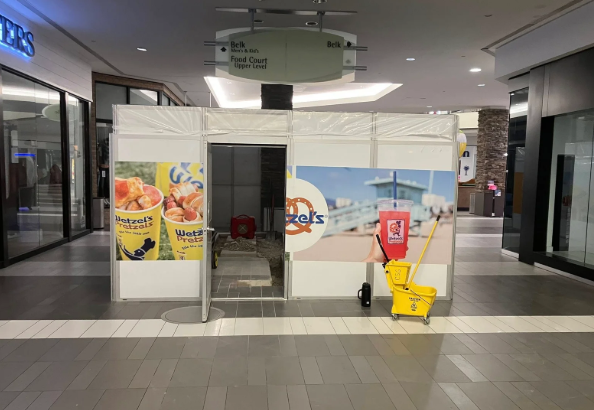 Empty mall storefront with a closed glass entrance, fruit ads, and a yellow caution wet-floor sign.