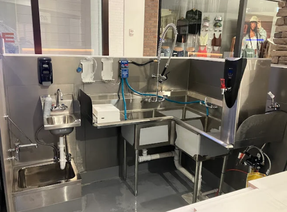 Commercial kitchen dishwashing station with stainless steel sinks, sprayer, and countertop equipment