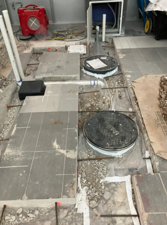 Damaged tiled floor with exposed holes, circular covers, and construction debris in an indoor space