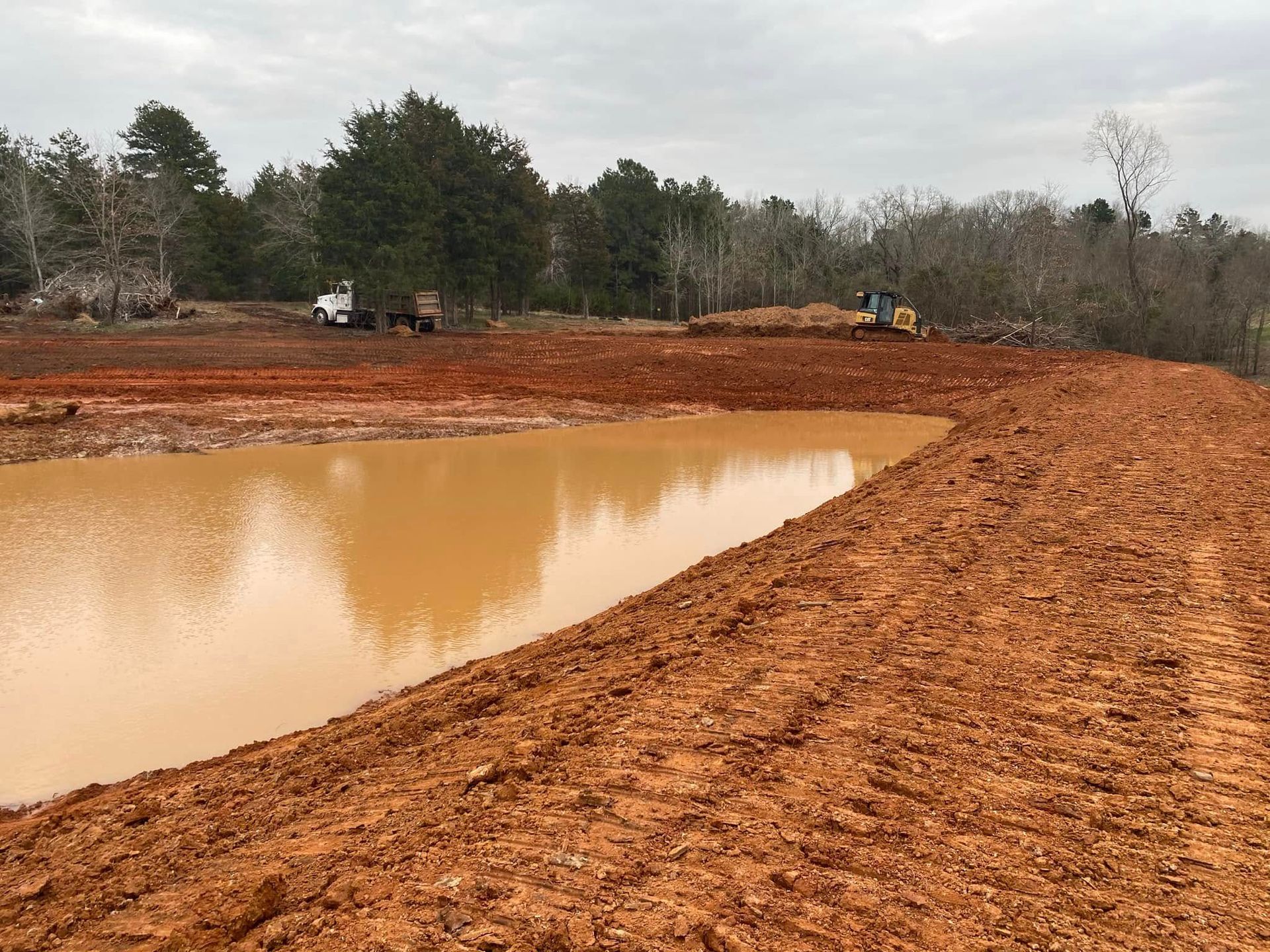 Mud-filled construction site with a large muddy pond and excavators in the background