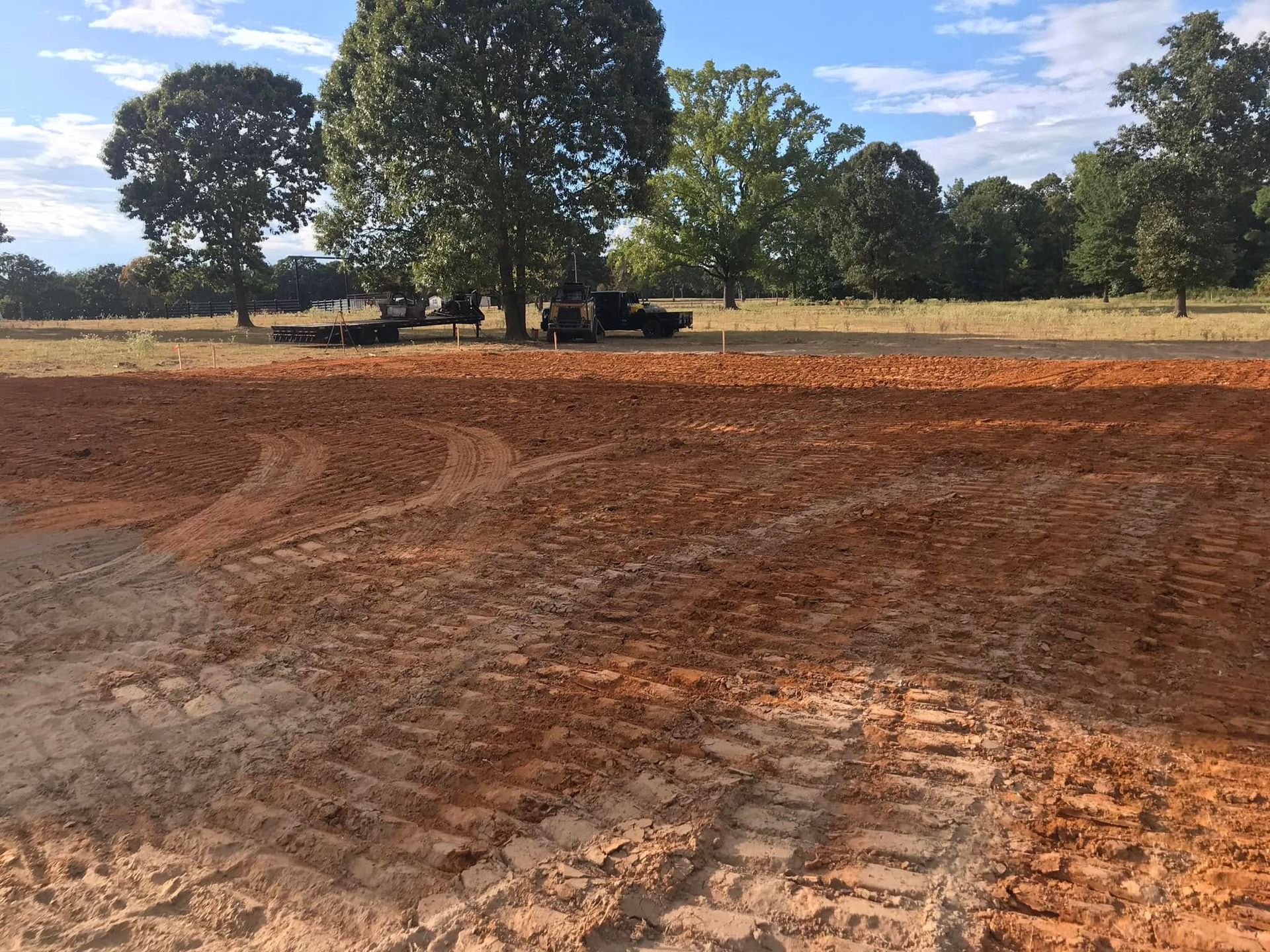 Freshly plowed red dirt field with tire tracks and trees in the background under a clear sky