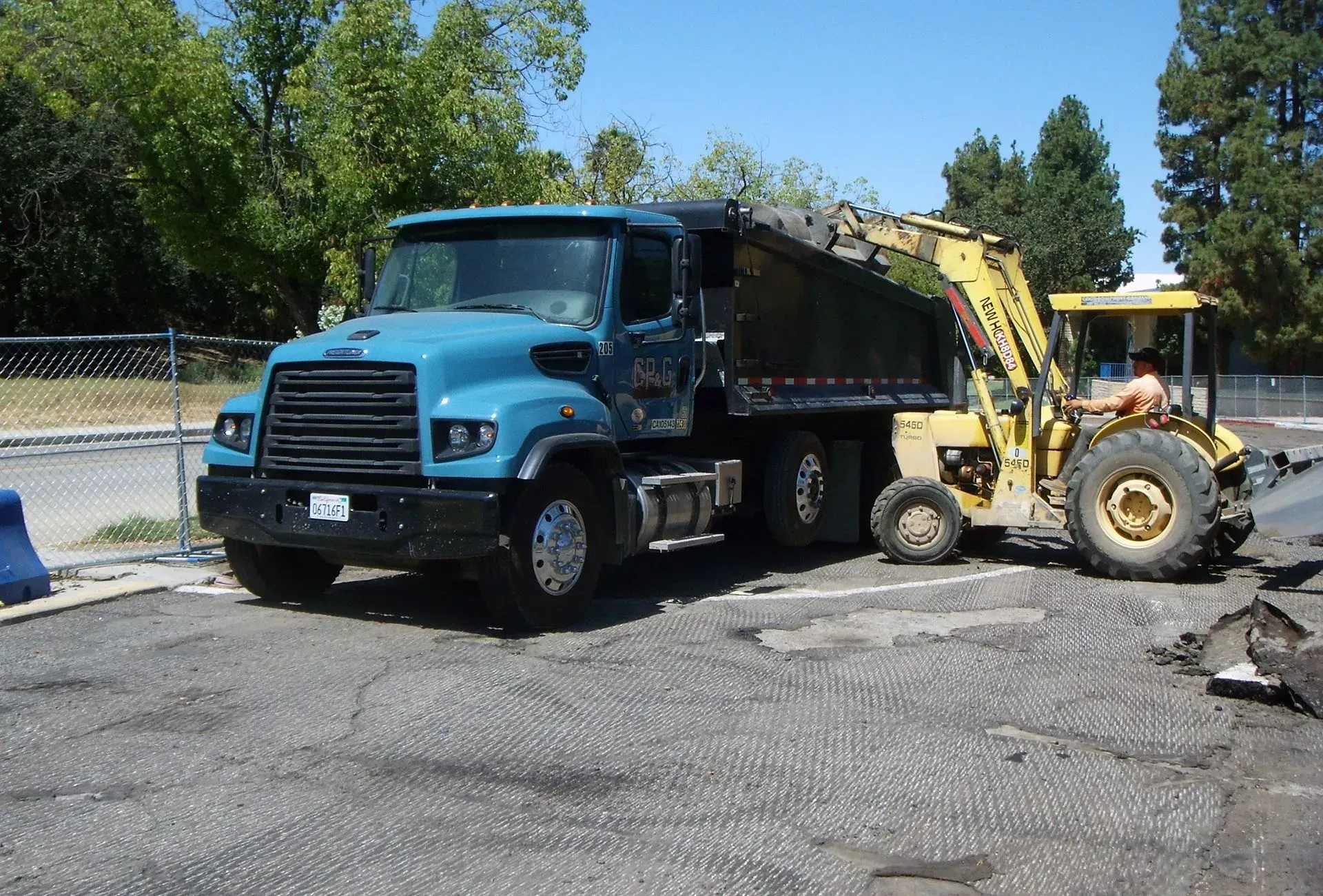 Blue dump truck and yellow backhoe parked on a gravel lot under a clear sky.