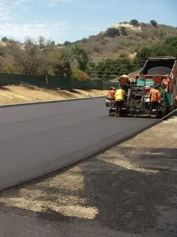 Road crew paving a black asphalt road with a paving machine on a hillside.
