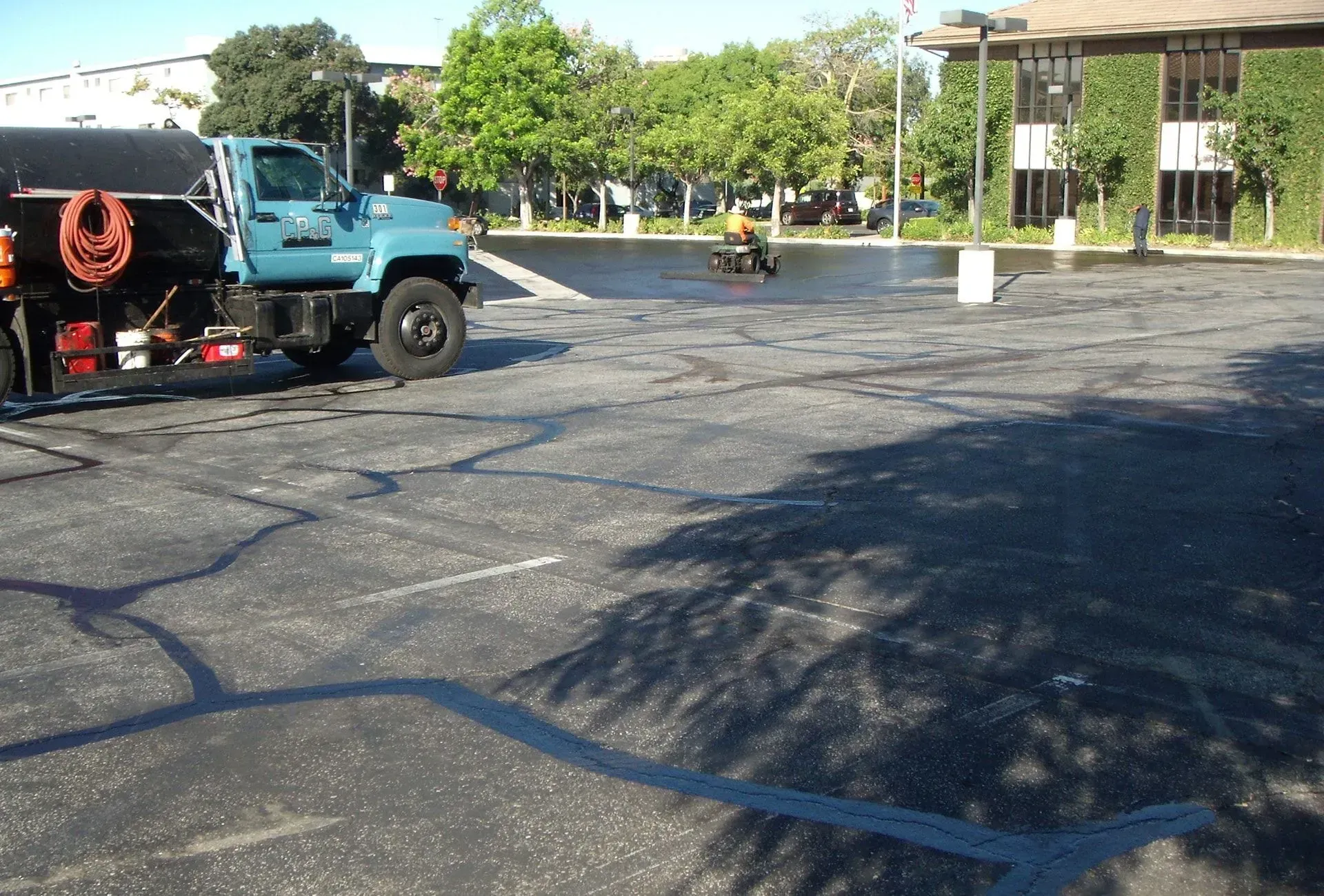 Blue utility truck on a sunlit paved lot near a building and trees