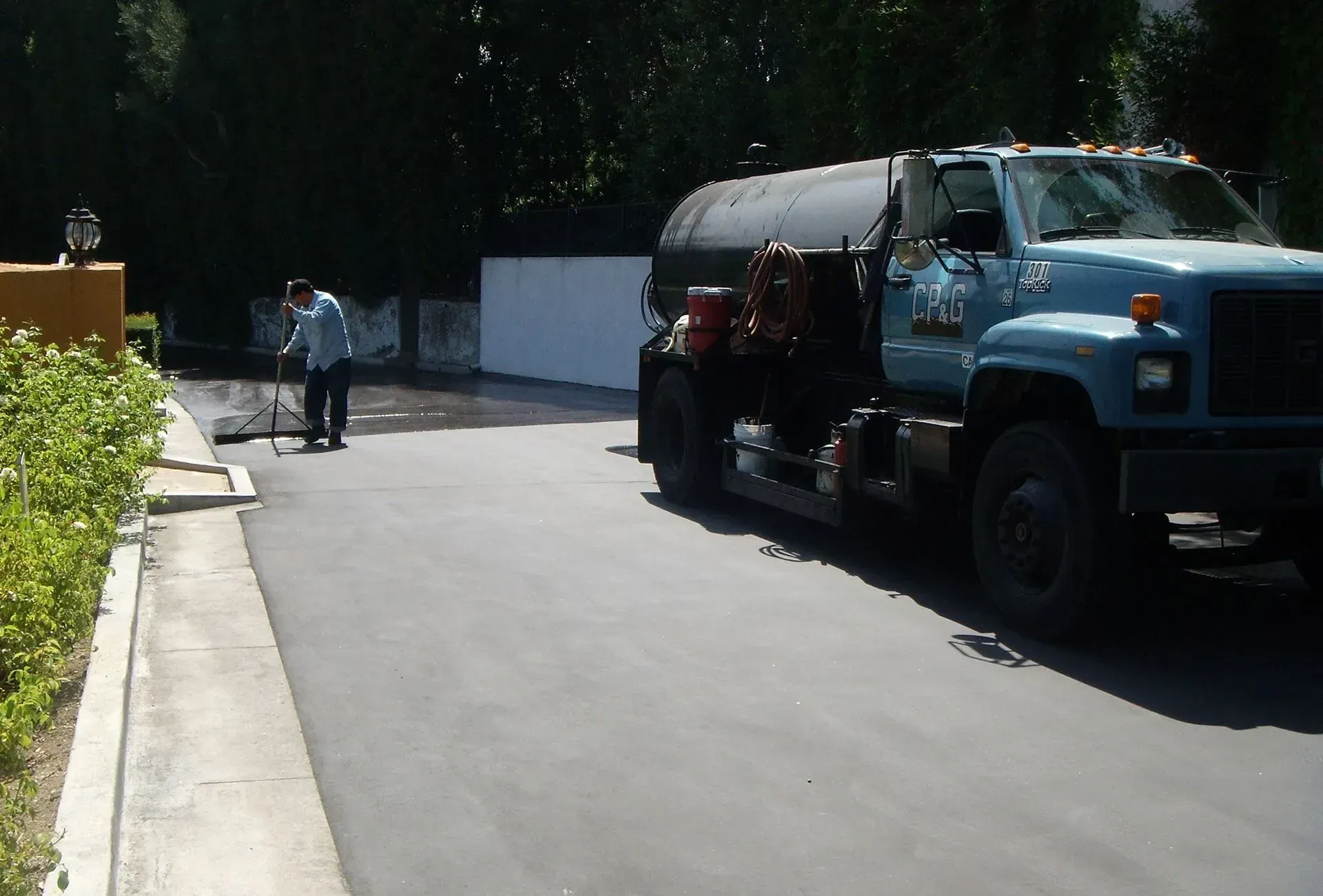 Large blue truck parked on a driveway beside a person walking in the sunlight