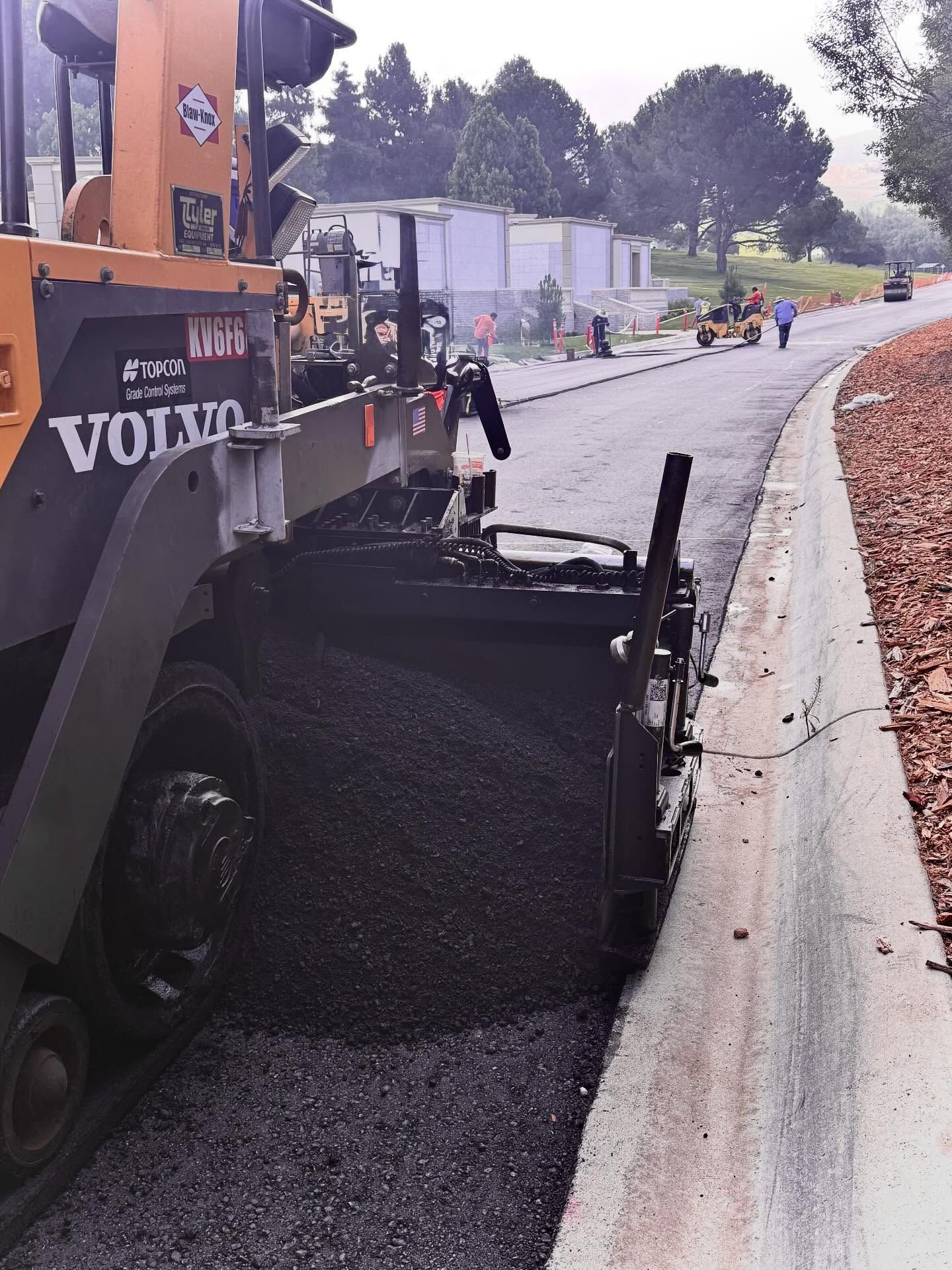 Orange asphalt paver laying black asphalt on a curbside road under construction