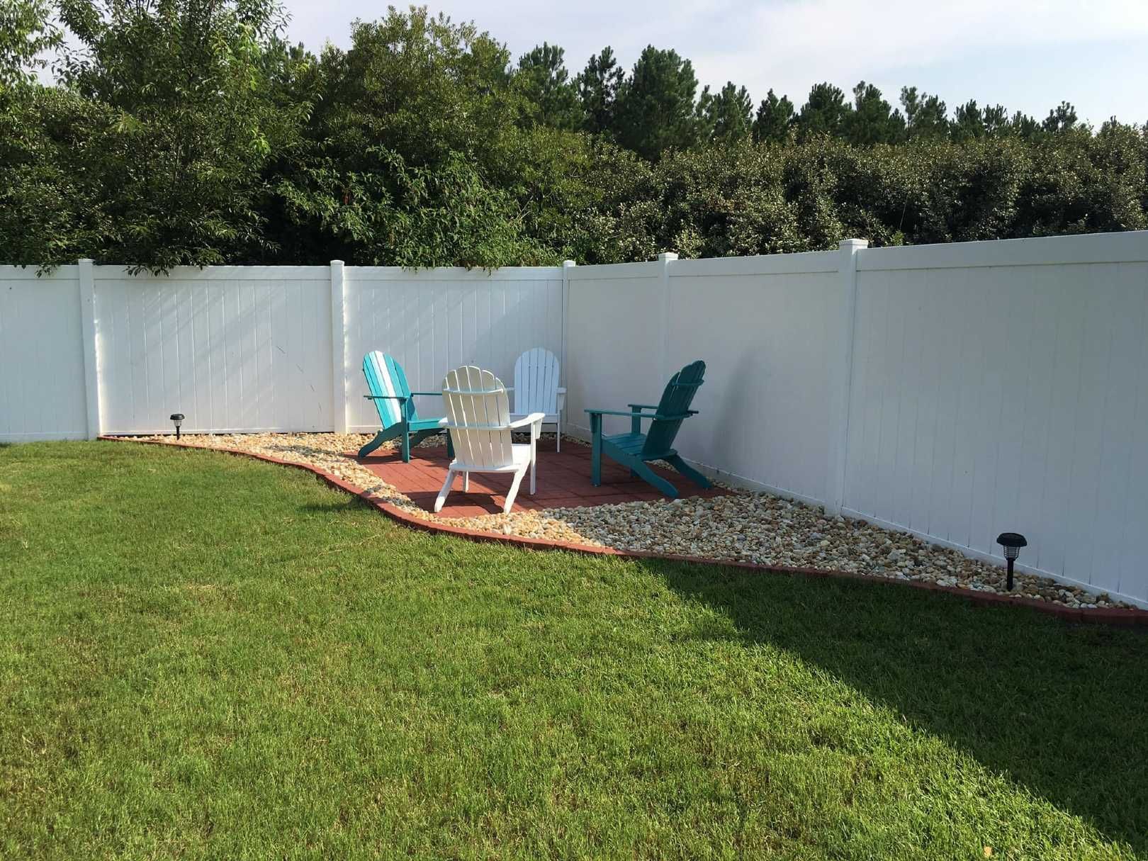 A backyard with lawn chairs and a white fence.