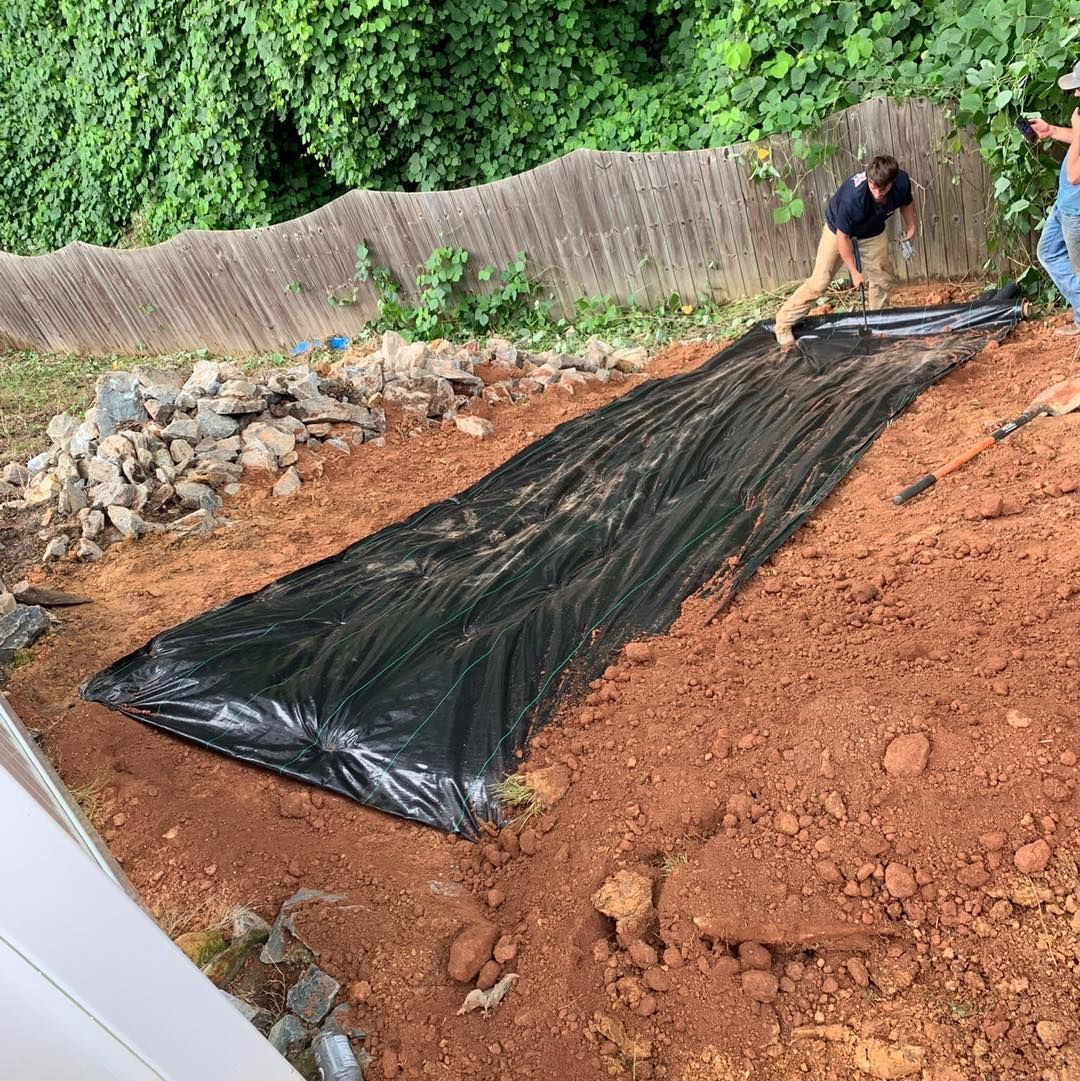 A man is laying a black tarp on top of a pile of dirt.