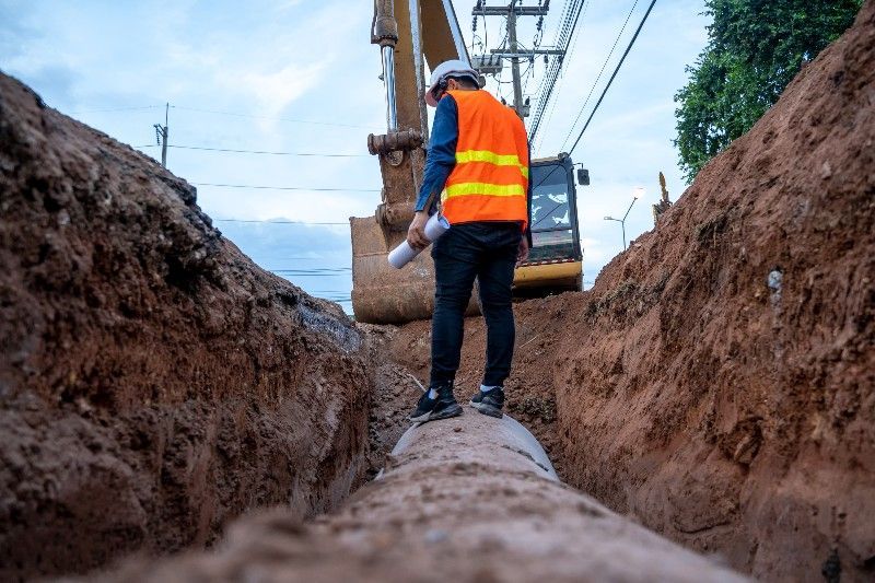 A construction worker is standing next to a pipe in a trench.