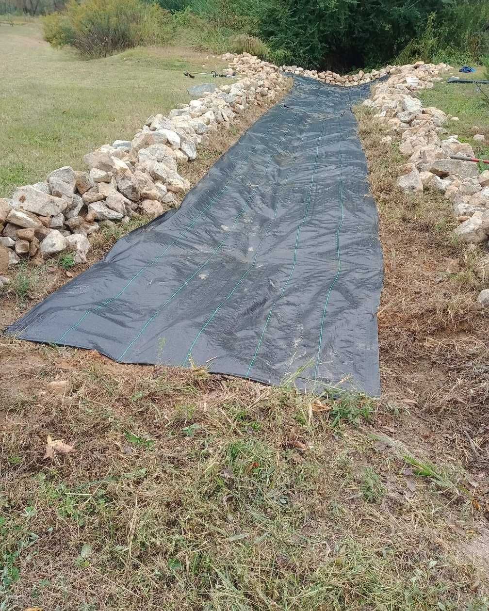 A black tarp is laying on the ground next to a stone wall.