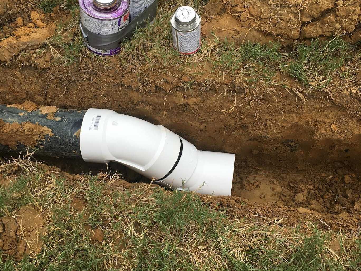 A white pipe is sitting in the dirt next to a bottle of spray paint.