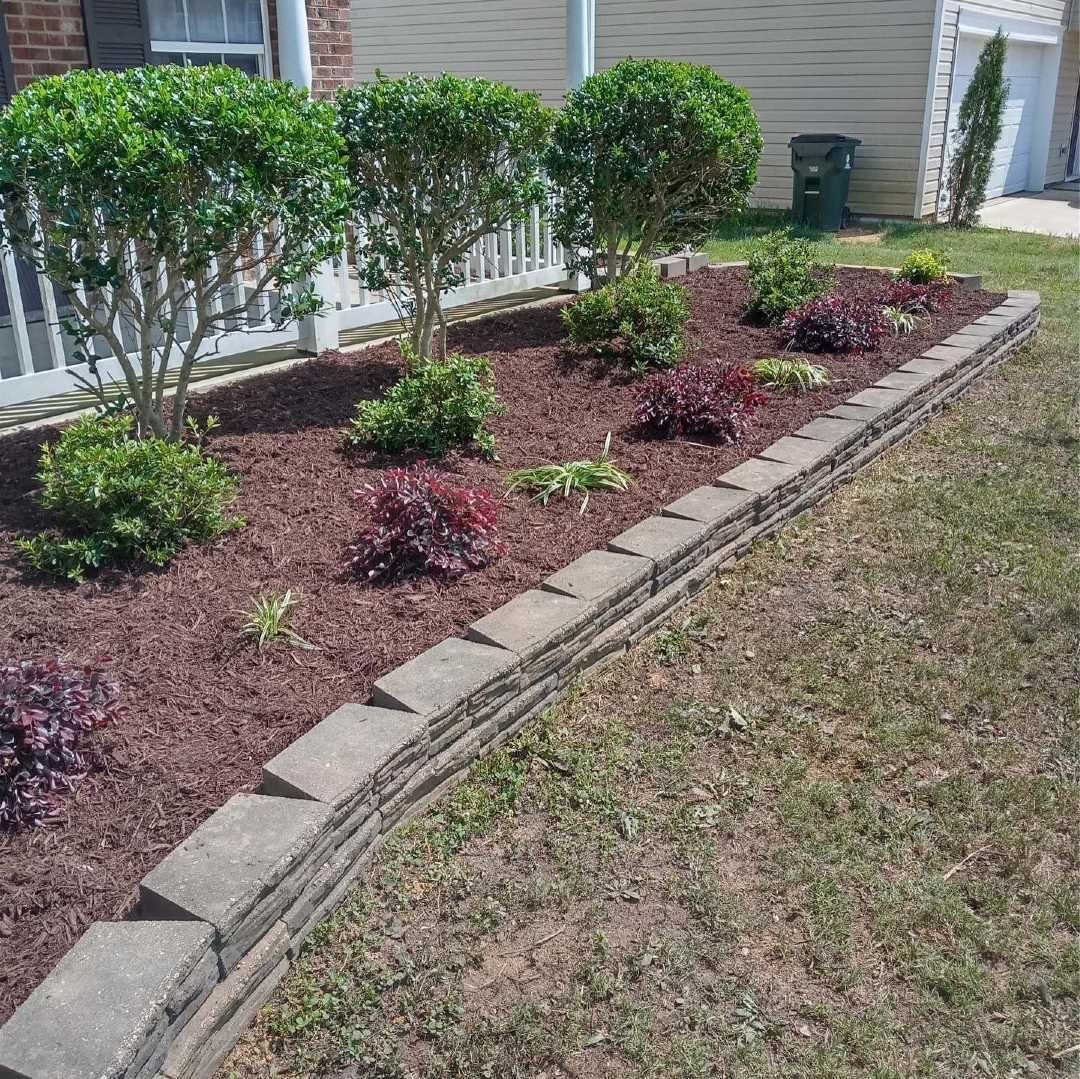 A lush green lawn with a stone border and a fence in the background.
