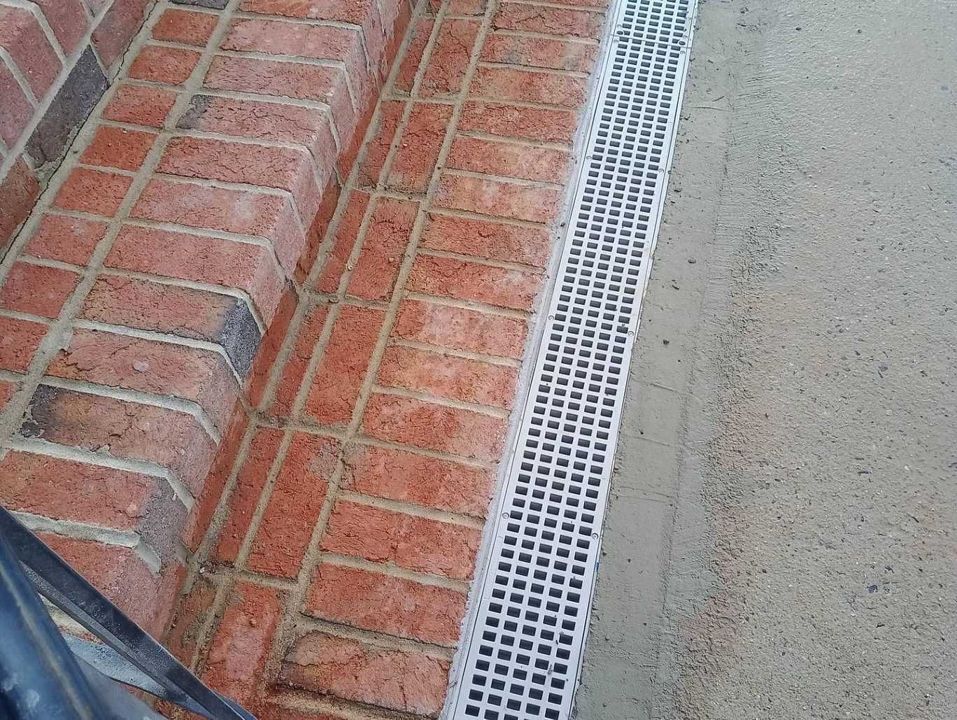 A brick wall with a white drain on the side of it.