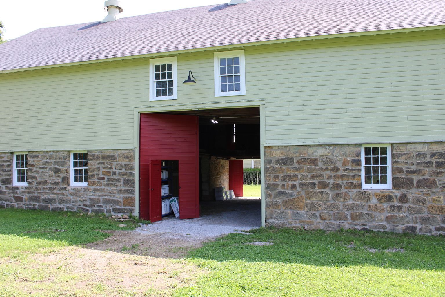 Barn with red doors and stone base, green siding, and white-framed windows.