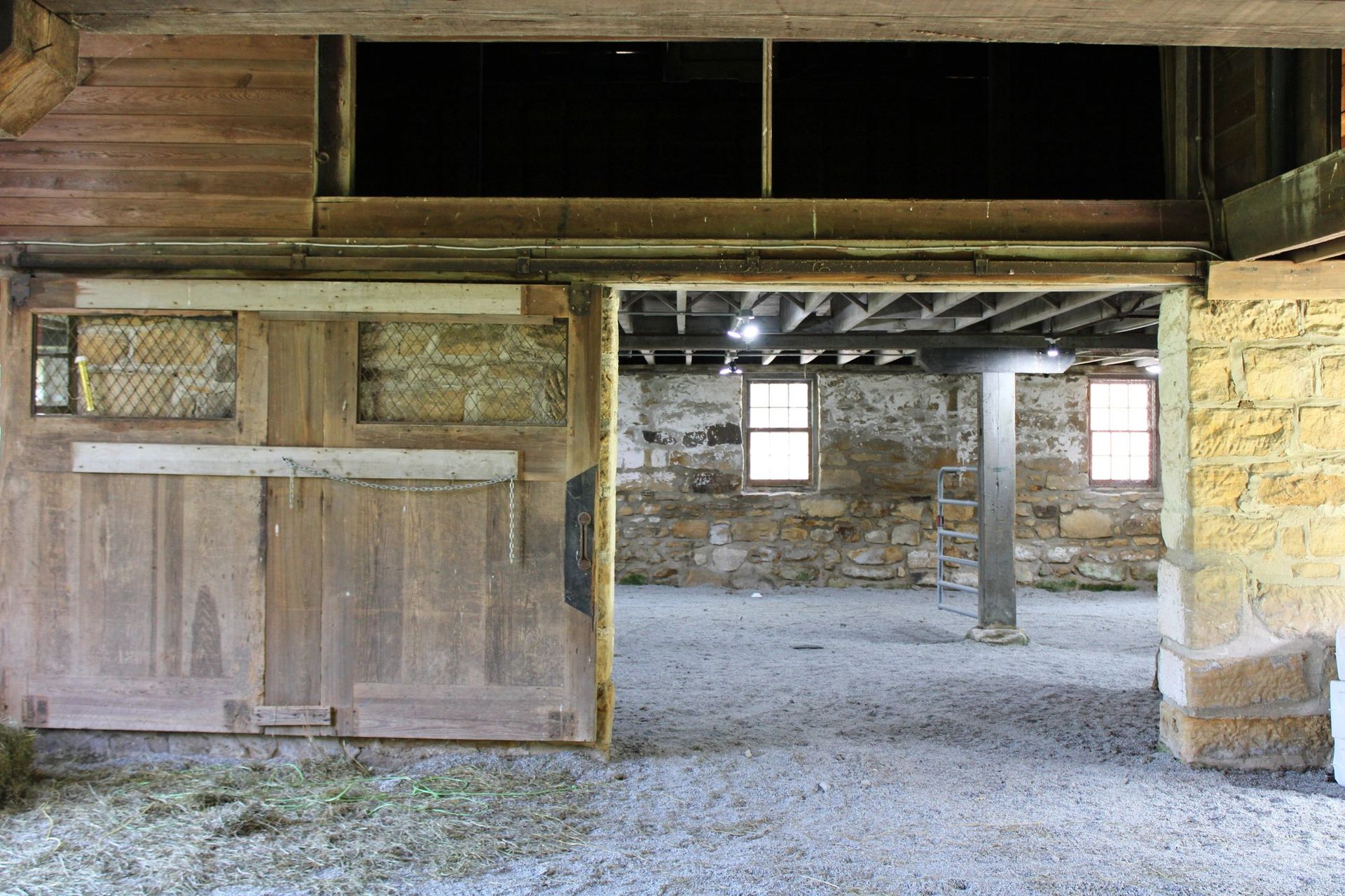 Open wooden barn door revealing a stone interior, with windows and a central support beam.